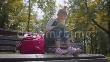 合上小美丽的学校女孩用彩色铅笔画画，<strong>坐在</strong>阳光明媚的<strong>公园里</strong>的长凳上。 慢动作镜头。